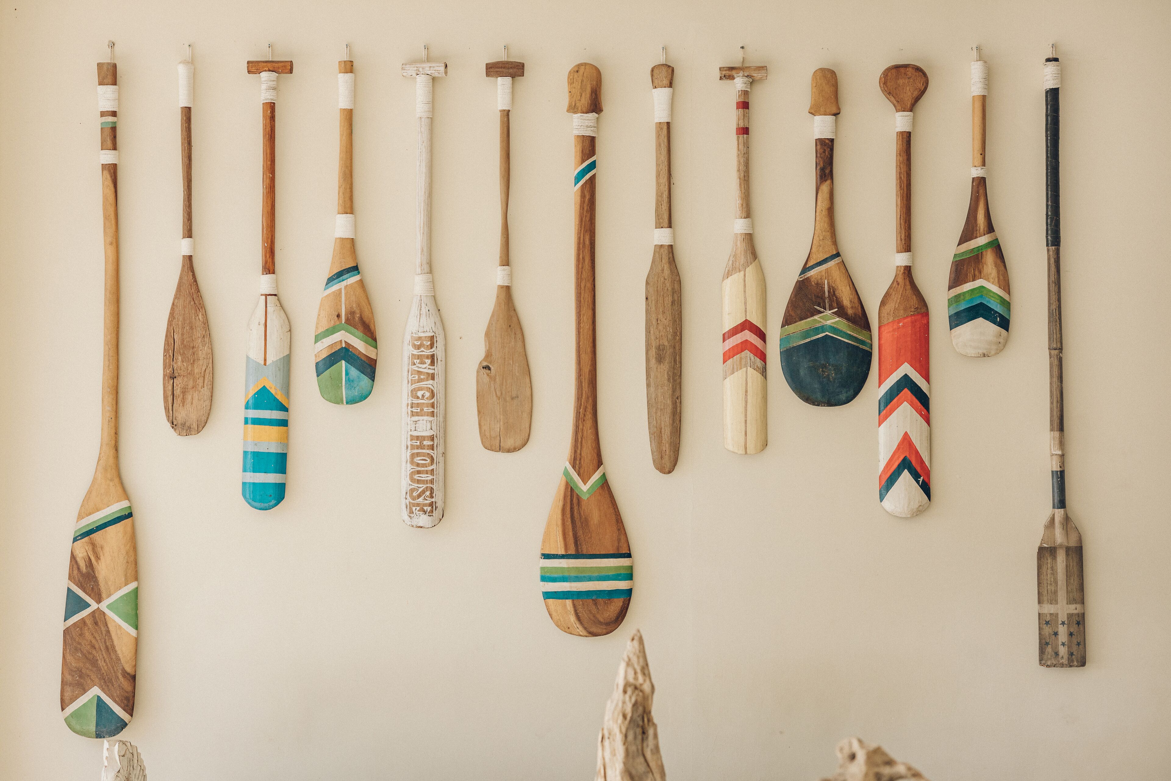A collection of wooden paddles with various designs and patterns, hanging on a wall.