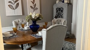 A dining room with a wooden table, upholstered chairs, a vase with flowers, and a hanging light fixture.