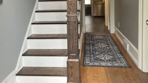 A staircase with wooden steps and a wooden balustrade, leading to a kitchen area with cabinets and a countertop.