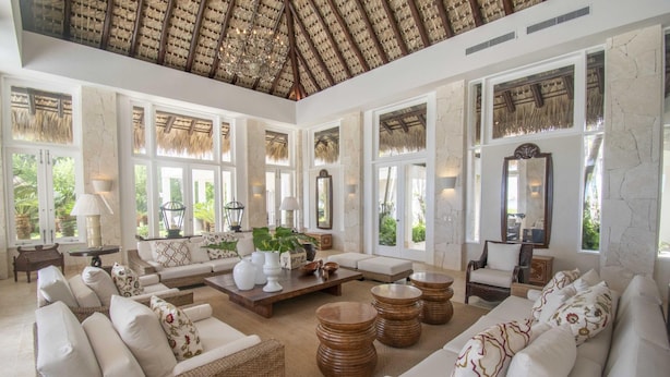 A spacious living room with wicker furniture, large windows, and a high ceiling with a thatched roof. - Ocean Front Luxury Villa in Golf and Beach Resort (Punta Cana)