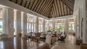 A spacious room with a high ceiling, large windows, and a central seating area with a dining table. - Ocean Front Luxury Villa in Golf and Beach Resort (Punta Cana)