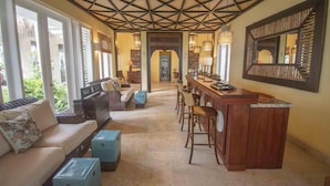 A spacious living area with a high ceiling, a cozy seating area, a bar with stools, and a large mirror. - Ocean Front Luxury Villa in Golf and Beach Resort (Punta Cana)