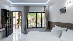 A modern hotel room with a large bed, a TV, and a balcony with curtains. - Coastal Village PQ (Phu Quoc)