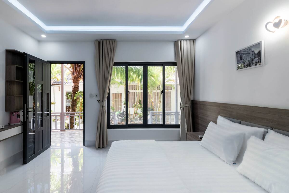 A modern hotel room with a large bed, a TV, and a balcony with curtains.