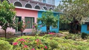 A multi-story building with balconies and a garden area with pink flowering plants. - Coastal Village PQ (Phu Quoc)
