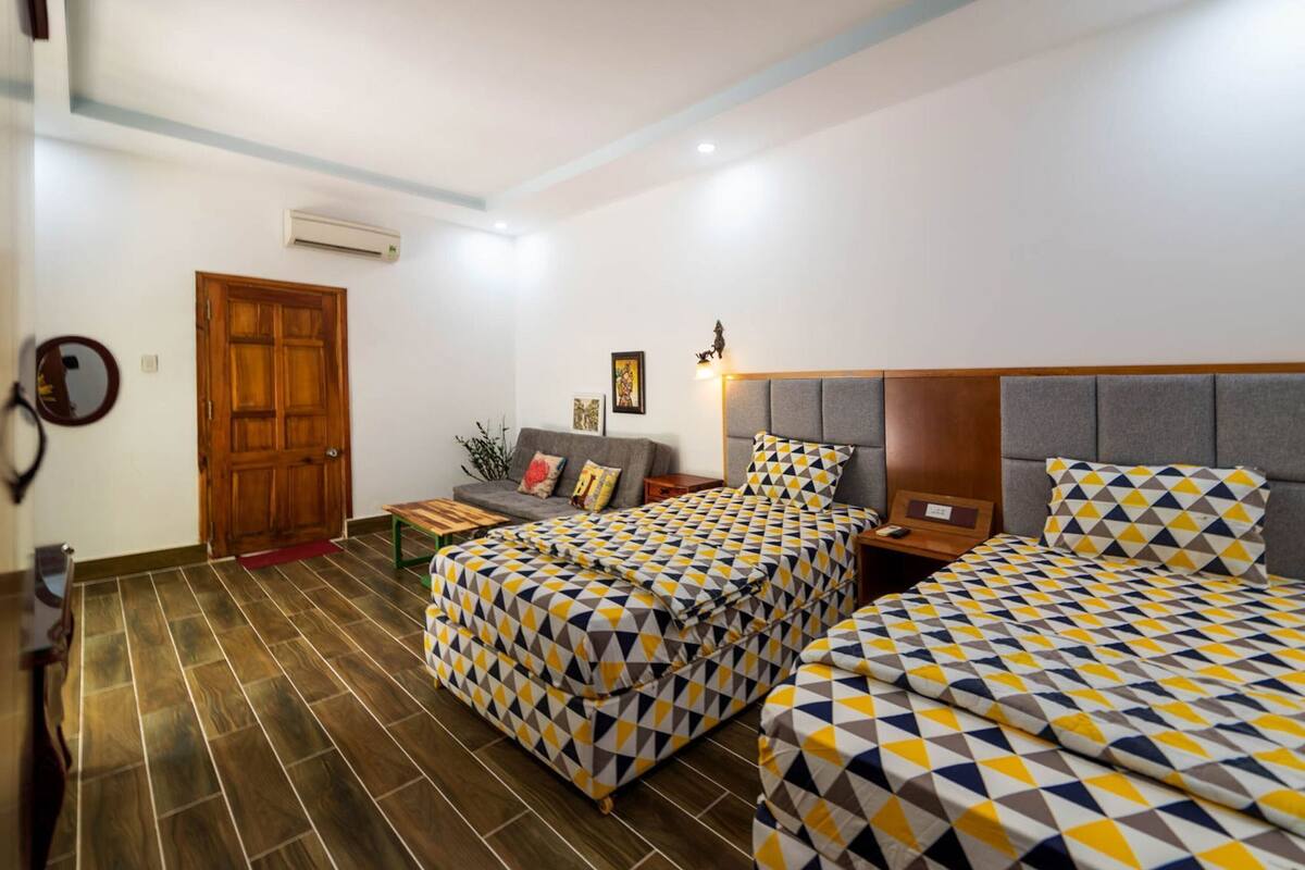 A hotel room with two beds, a sofa, a wooden door, and a mirror.
