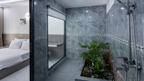 A modern bathroom with a shower, a glass-enclosed toilet, and a bed with white bedding. - Coastal Village PQ (Phu Quoc)