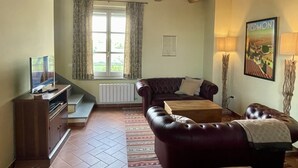 Uma sala de estar com um sofá de couro marrom, uma mesa de centro de madeira, uma televisão e uma janela com cortinas.