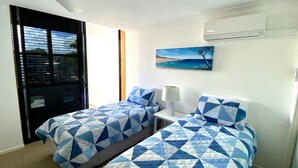 A hotel room with two beds, a painting of a beach, and an air conditioning unit.