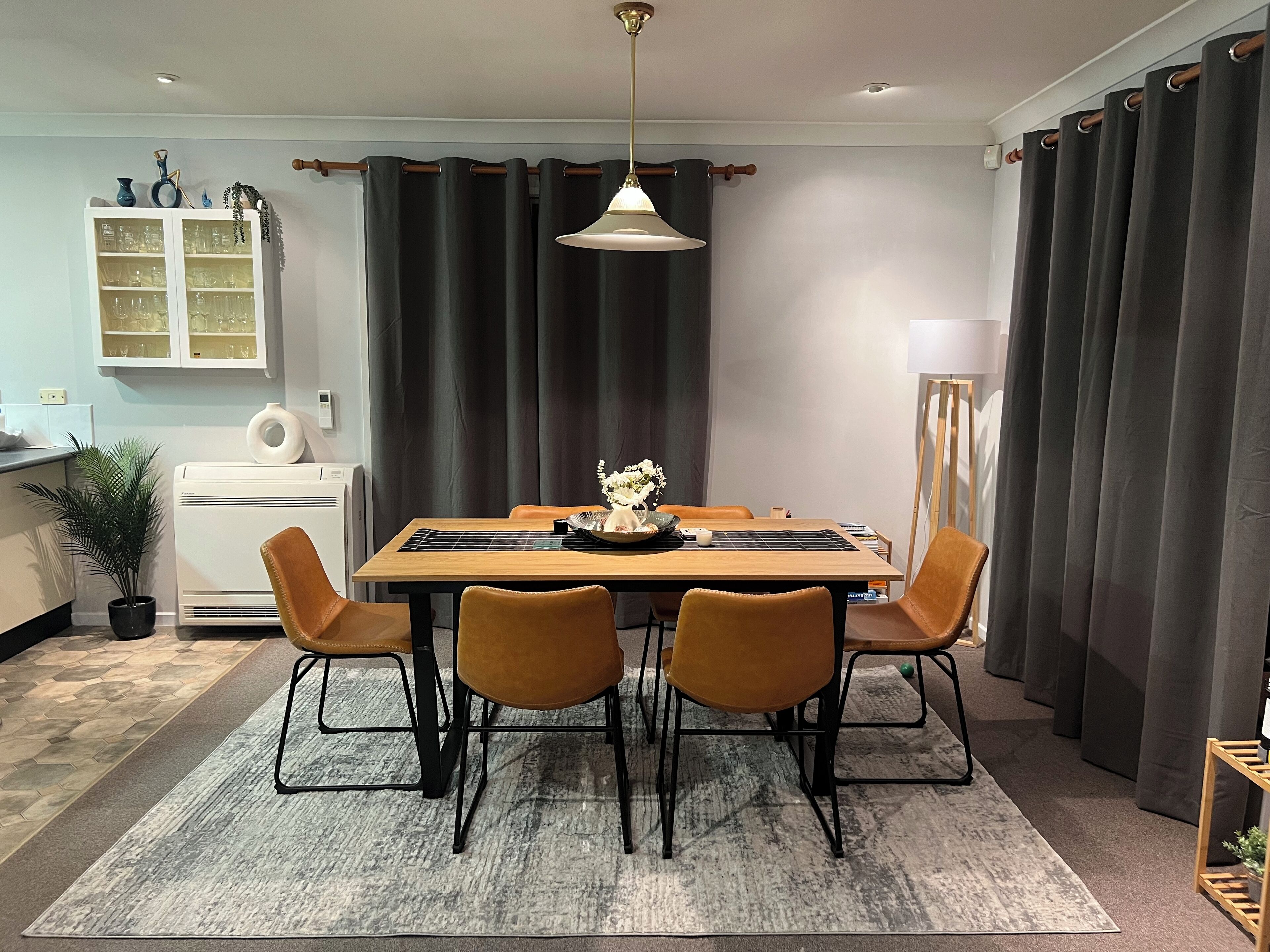 A dining area with a wooden table, four chairs, a vase with flowers, and a pendant light.