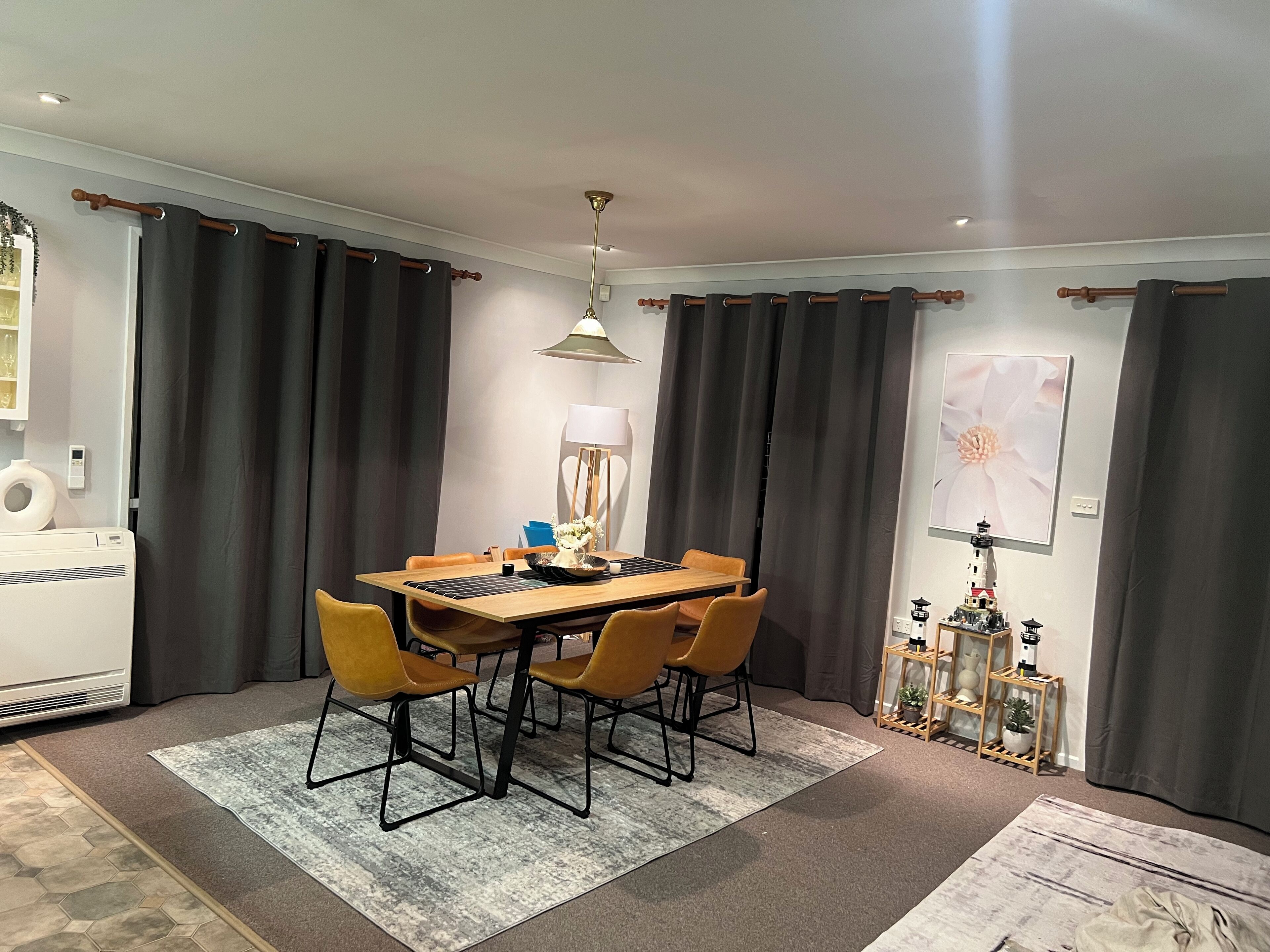 A dining area with a wooden table, four chairs, a rug, a lamp, and a wall-mounted picture.