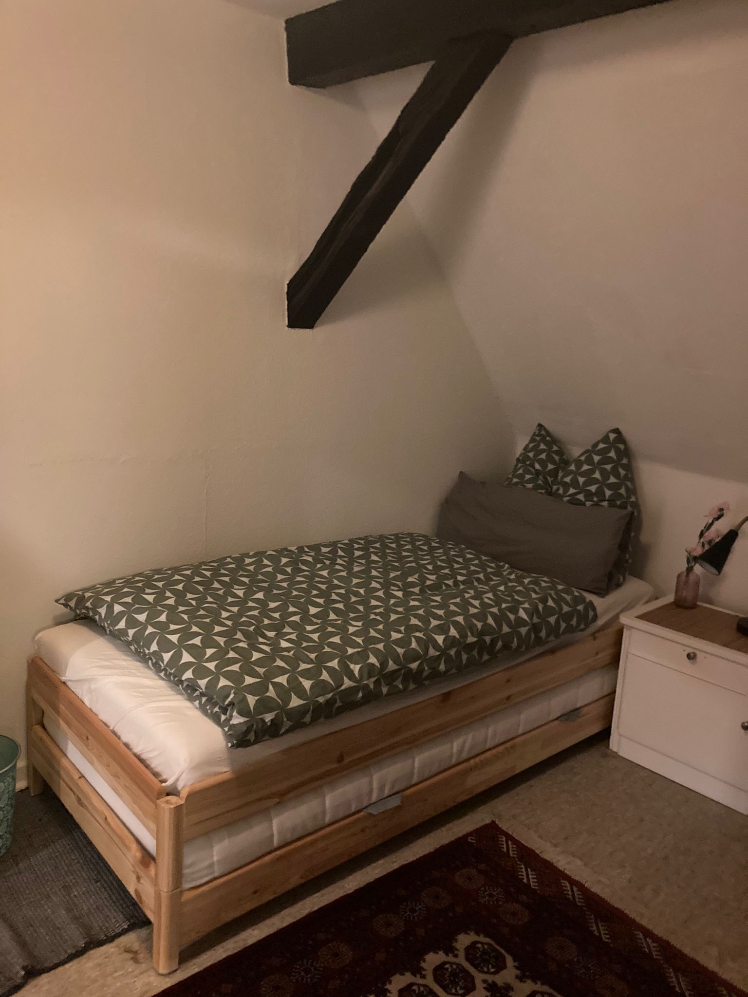 A small, cozy bedroom with a wooden bed, a nightstand, and a patterned rug.
