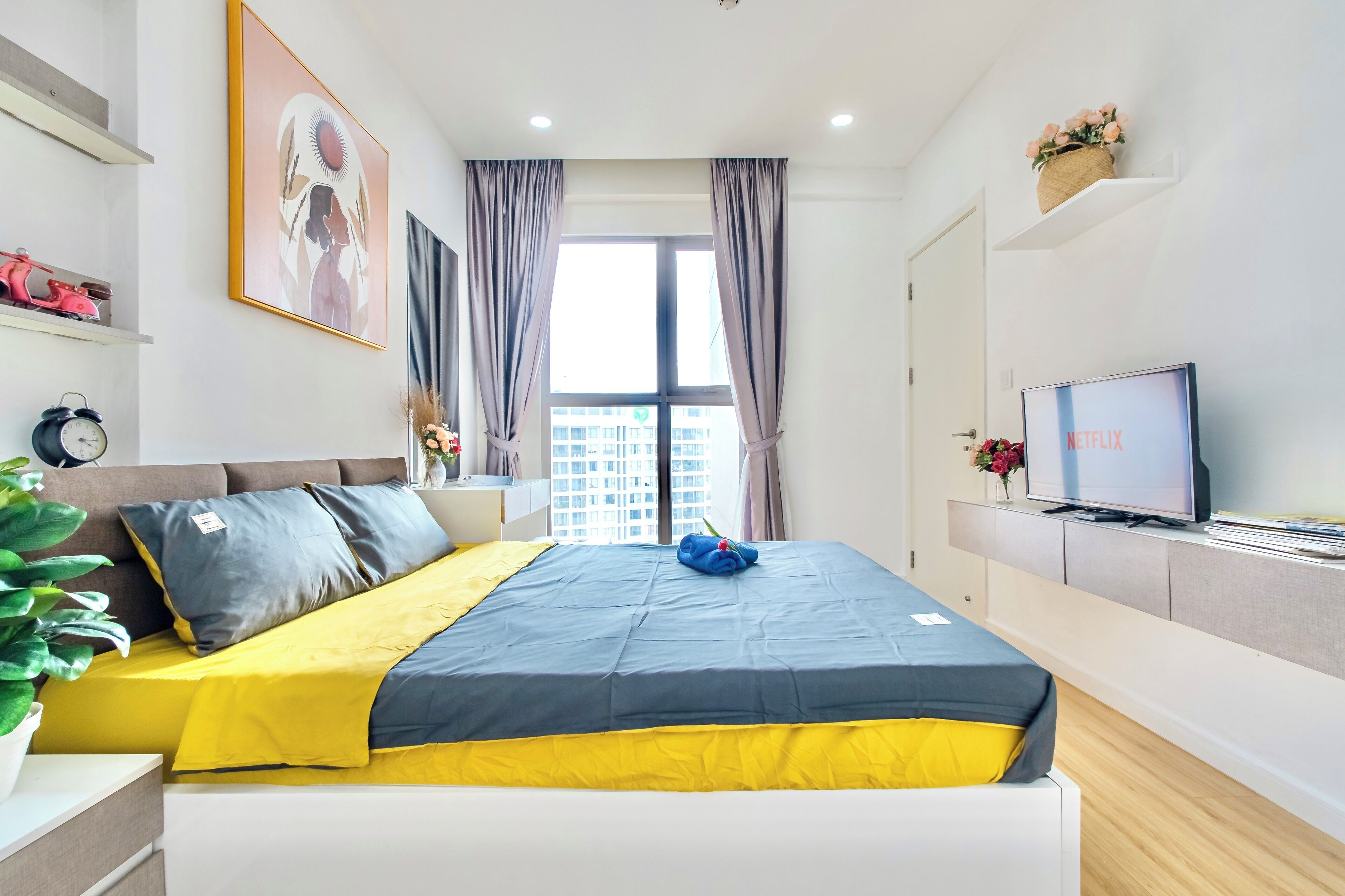 A modern hotel room with a bed, a TV, a window with curtains, and a plant.