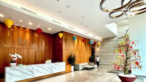 A modern reception area with a marble reception desk, wooden panel walls, and a large potted plant with red and yellow flowers.