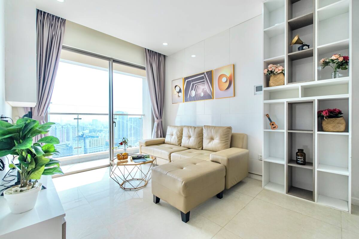 A modern living room with a beige sectional sofa, a coffee table, and a white shelving unit with decorative items.