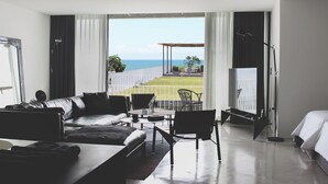 Una habitación de hotel moderna con una cama grande, un sofá, una mesa de comedor y vista al mar.