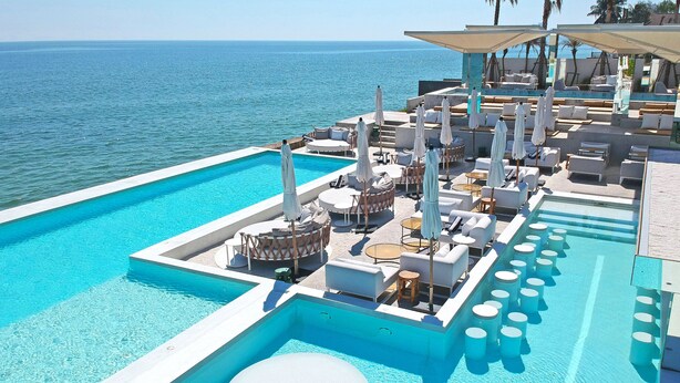 Zona de piscina con sillones, sombrillas y vista al mar.