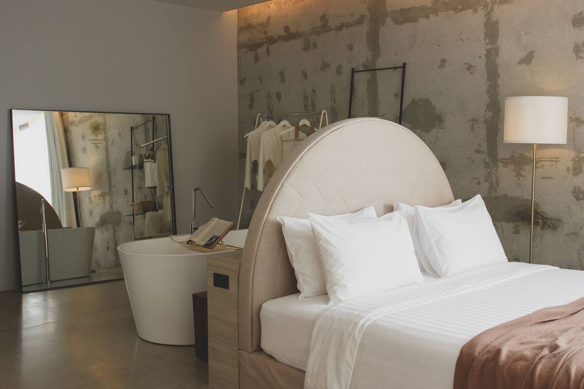 A modern hotel room with a large bed, a round bedside table, a mirror, and a wardrobe with hanging clothes.