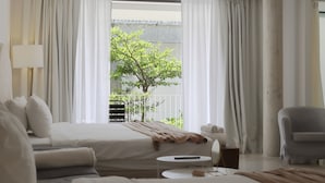 Habitación de hotel con cama, sofá, sillón, una mesita y vistas a un árbol y balcón.