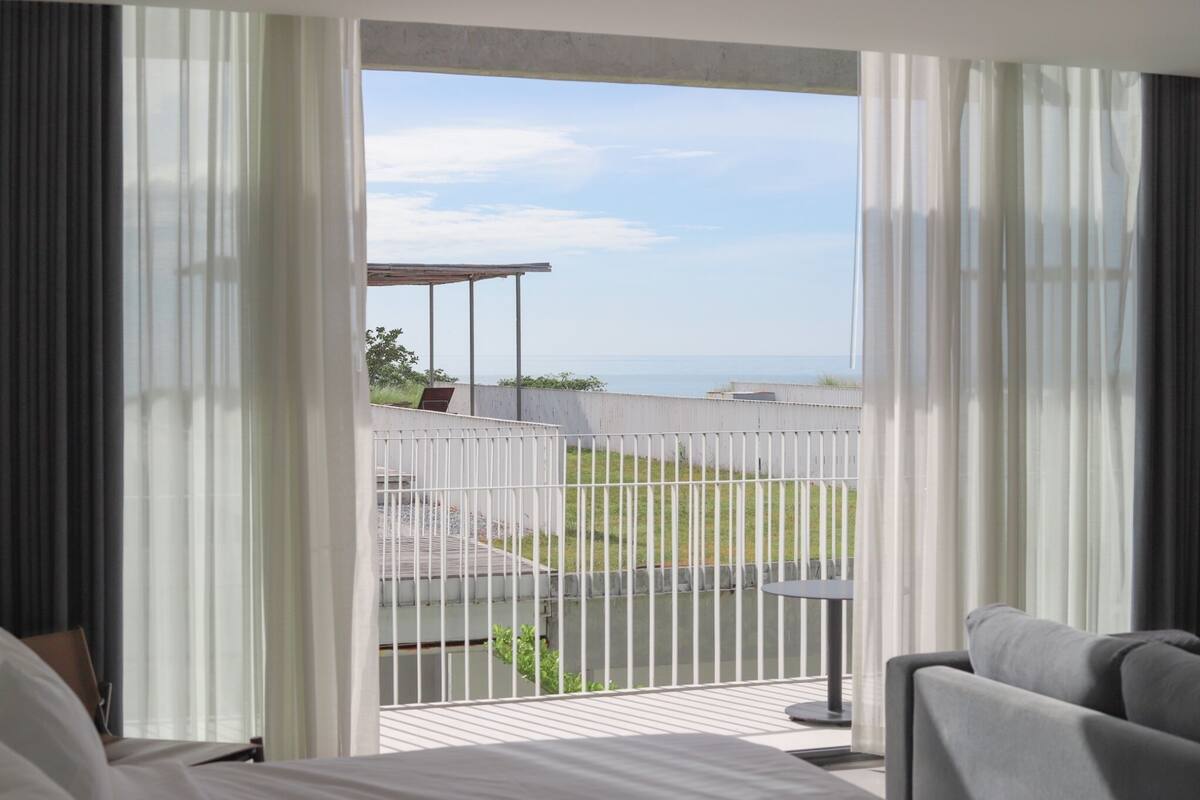 A balcony with a view of the sea, a covered seating area, and a small table.