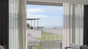 Un balcón con vista al mar, una zona de estar techada y una mesa pequeña.