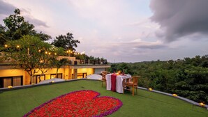 Terraço no telhado com arranjo floral em formato de coração, mesa de jantar com cadeiras e vista para o verde ao redor.