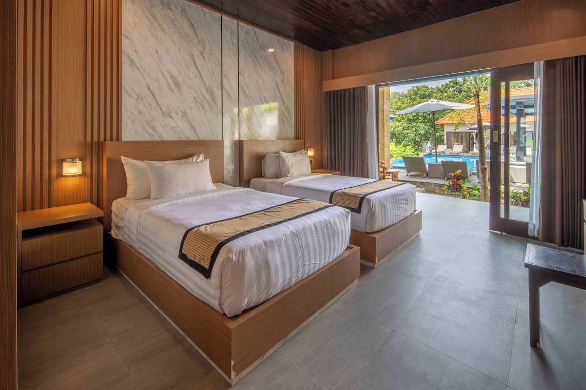 A hotel room with two beds, wooden headboards, marble wall, and a view of the pool area.
