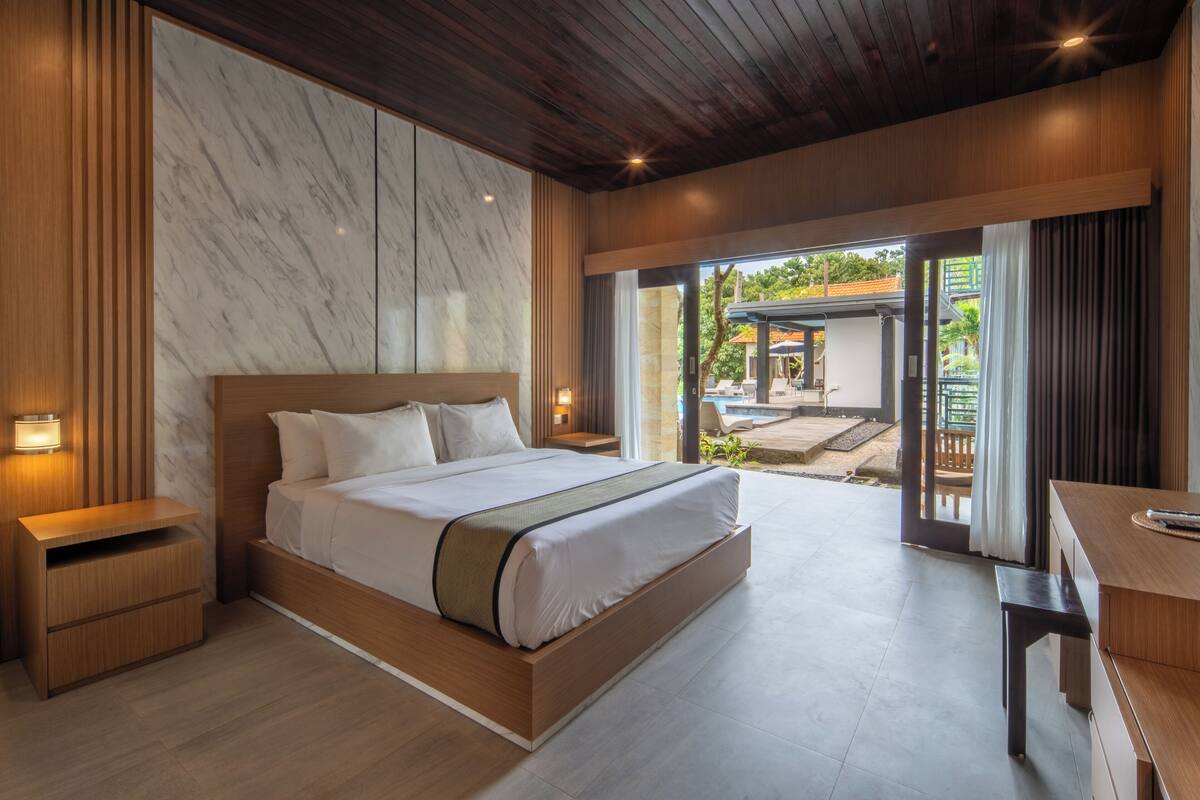 A modern bedroom with a large bed, wooden nightstands, a desk, and a view of the outdoor patio.