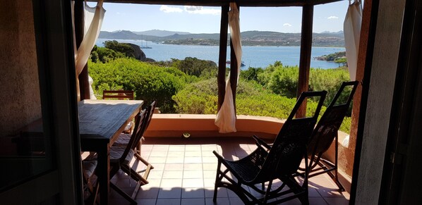 A balcony with a table and chairs, overlooking a scenic view of a body of water and greenery.