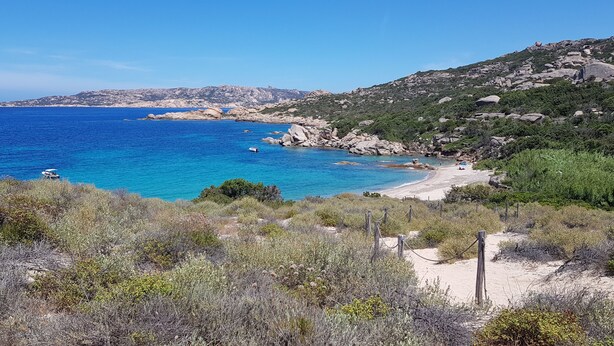 Ett kustlandskap med en sandstrand, klippiga utskjutande partier och gles vegetation.