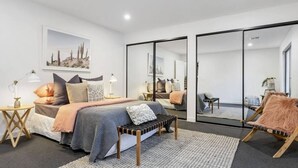 Un dormitorio moderno con una cama grande, un banco, una silla y un espejo.