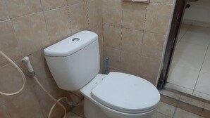 Un inodoro blanco estándar con tanque, asiento, una tubería visible y un pequeño estante rosa en la pared.