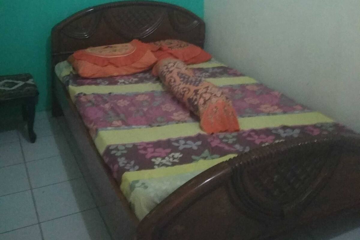 A single bed with a wooden headboard in a room with green walls and a tiled floor.