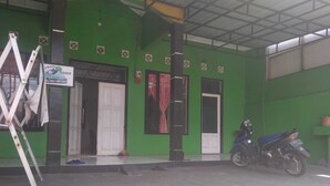 Un edificio verde con una puerta y ventanas blancas, una motocicleta estacionada afuera y una escalera al frente.