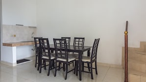 Een eetgedeelte met een rechthoekige tafel en zes stoelen, een klein keukeneiland en een trap met een decorale metalen leuning.