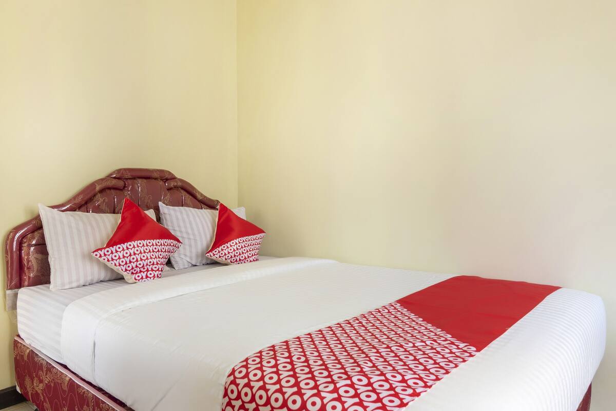 A bed with a white and red patterned bedspread, a wooden headboard, and striped pillows.