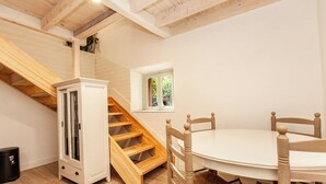 Une pièce avec un escalier en bois, une armoire blanche, une table ronde entourée de chaises et une fenêtre donnant sur un paysage verdoyant.