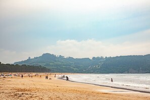 A beach with people walking along the shore and a forested hill in the background. - Cozy cottage besides a stream and a river (Villaviciosa)
