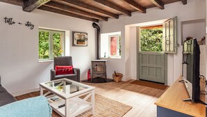 Un salon chaleureux avec un plafond en bois, une table basse en verre, un fauteuil rouge et une porte verte.