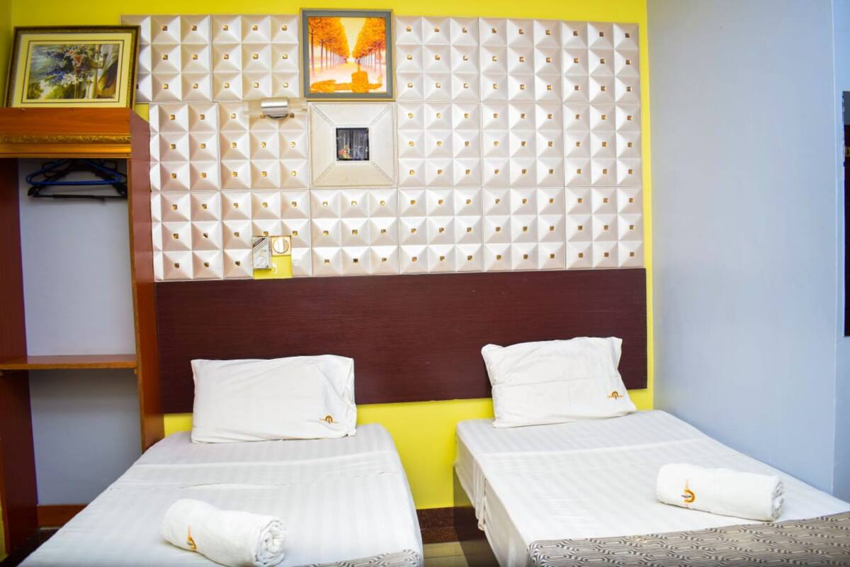 Une chambre d’hôtel avec deux lits simples, une tête de lit en bois, un panneau décoratif mural et une petite fenêtre.