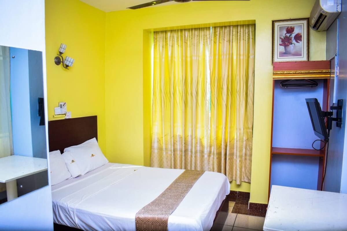 Une chambre d’hôtel avec un lit, un bureau, une chaise, une télévision et une fenêtre avec des rideaux.