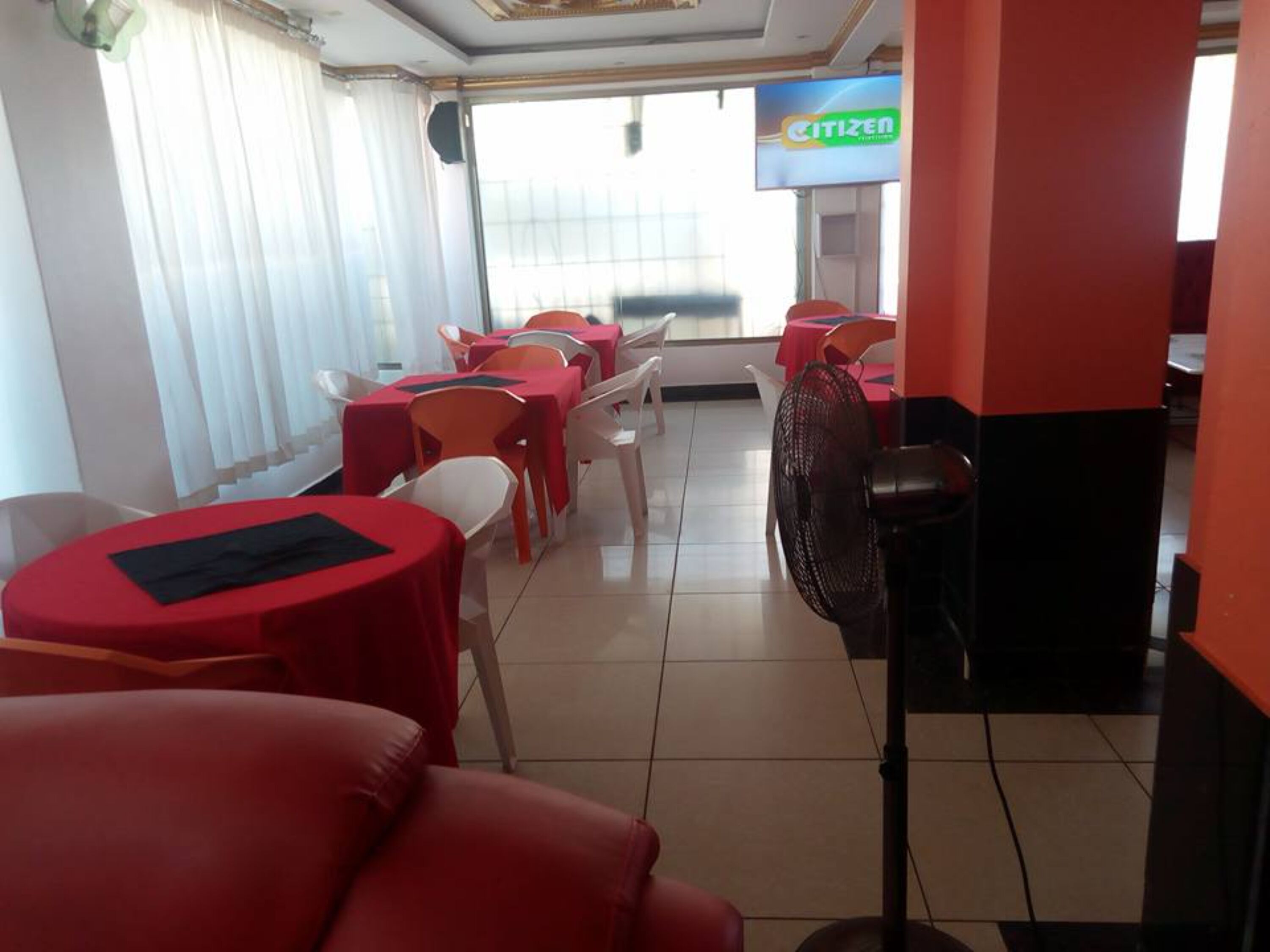 A dining area with red tables and chairs, a fan, and a 'CITIZEN' sign in the background.