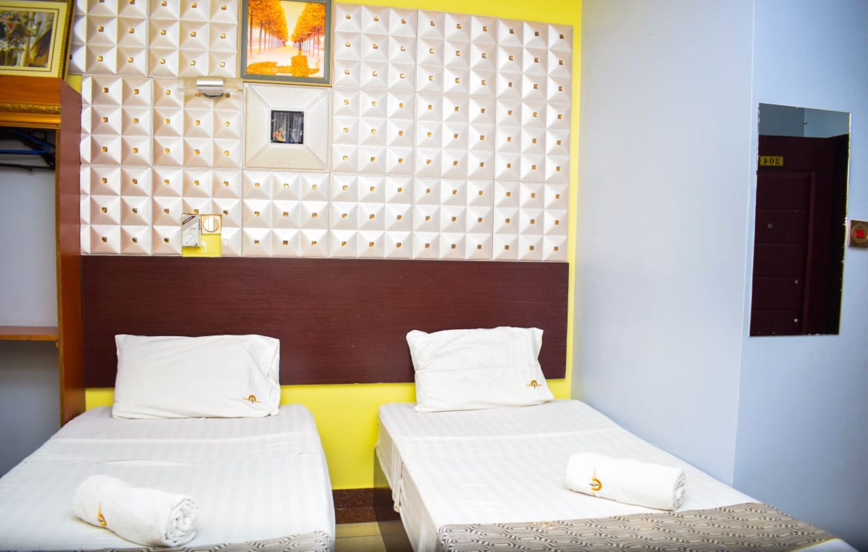Habitación de hotel con dos camas individuales, cabecera de madera y pared de acento amarilla.