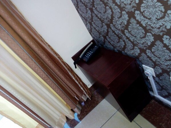A corner of a room with a patterned wallpaper, a telephone on a wooden table, and a curtain partially drawn. - Louis Montfort Grand Resort - Mombasa (Mombasa)