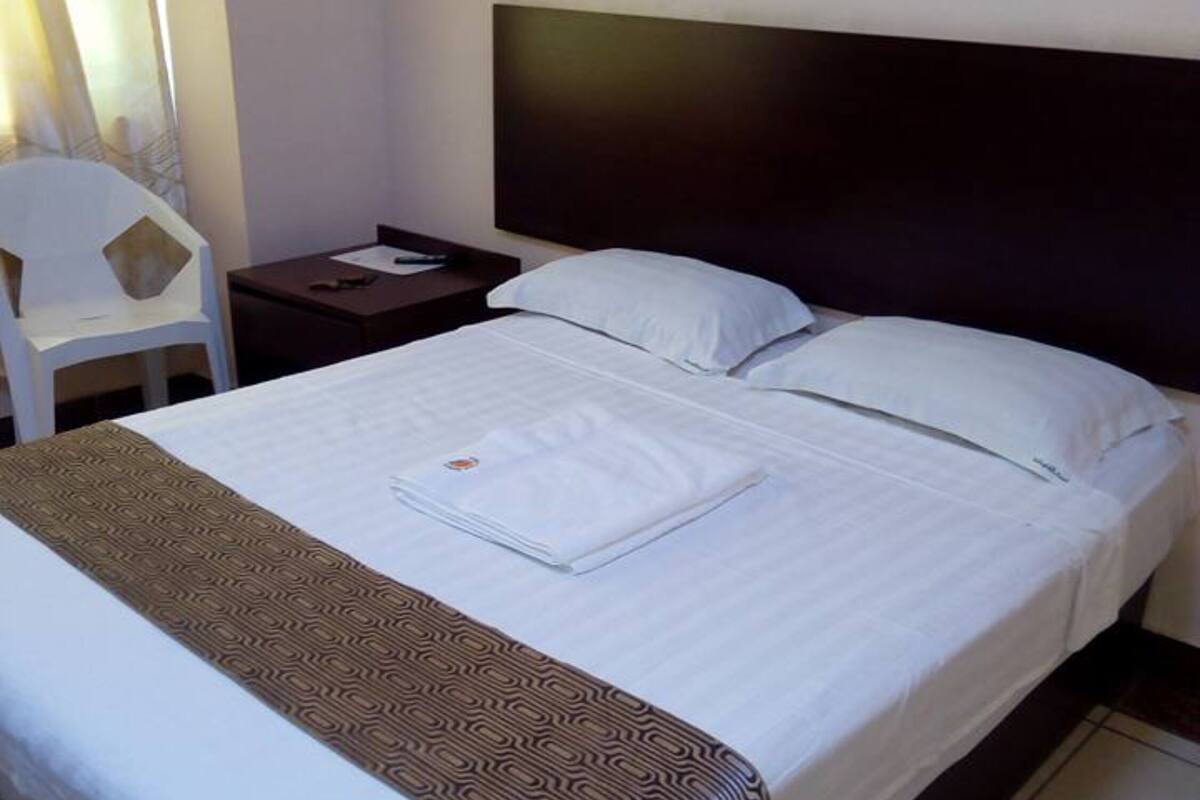 Une chambre d’hôtel avec un lit, une table de chevet, une chaise et une fenêtre avec des rideaux.