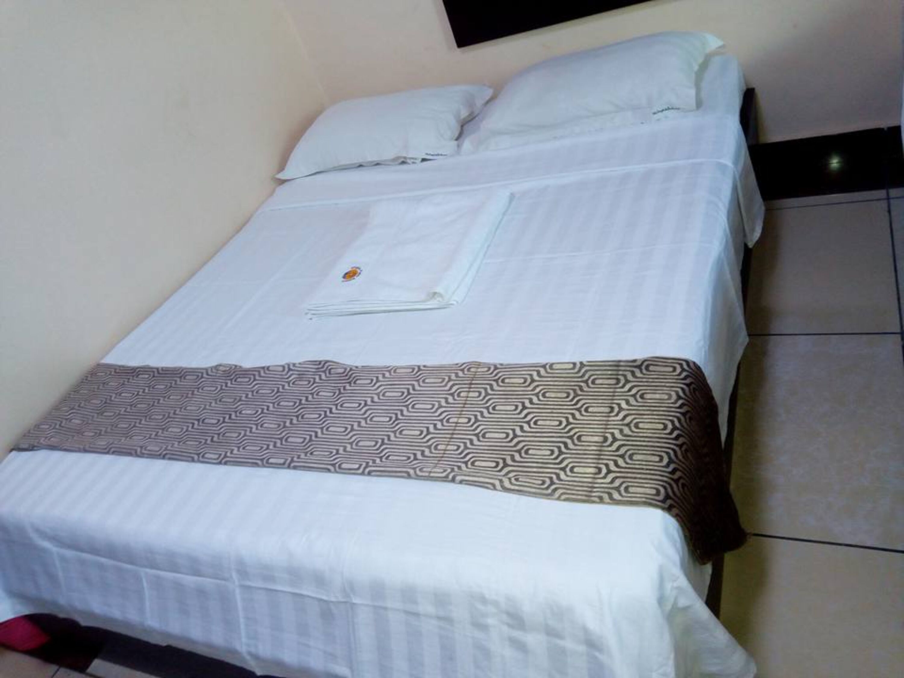 Una cama individual con una manta decorativa estampada, ropa de cama blanca y un pequeño adorno sobre la cama.