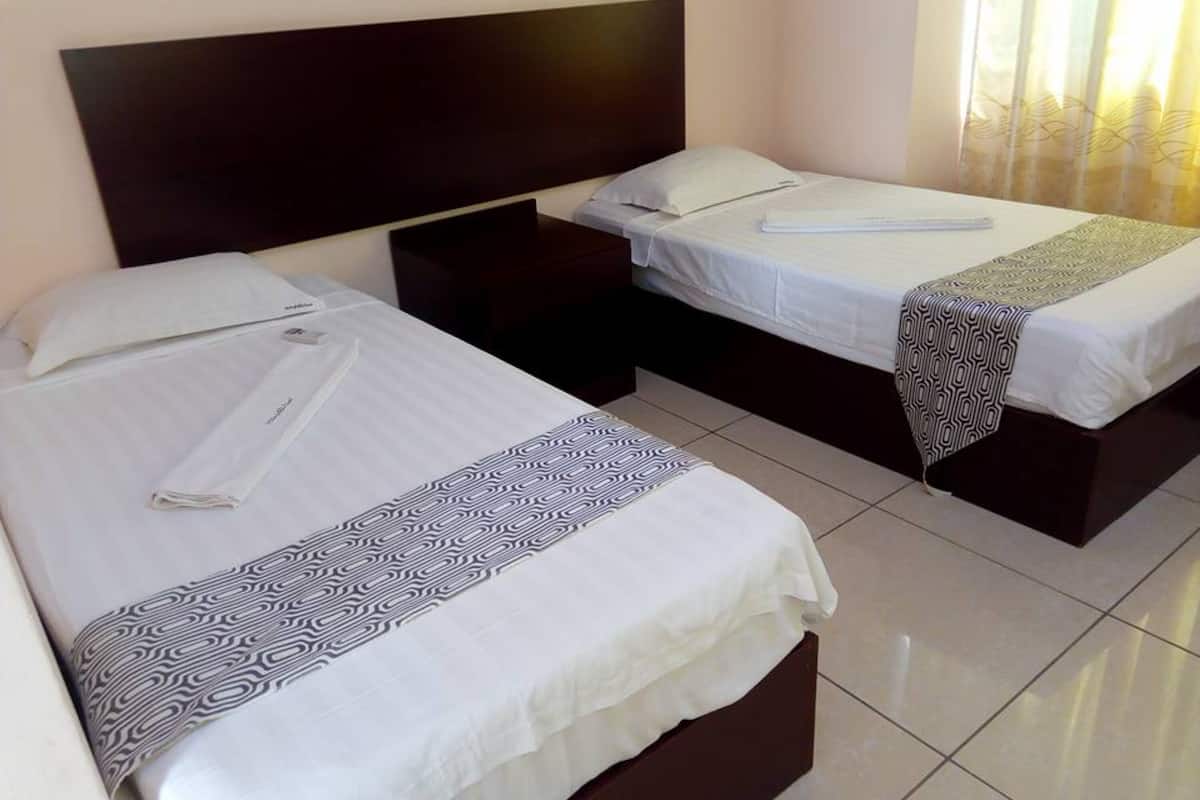 A hotel room with two beds, a dark headboard, a bedside table, and a window with curtains.
