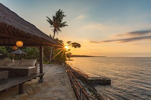 Relax on a wicker sofa under a thatched-roof structure overlooking the calm sea.