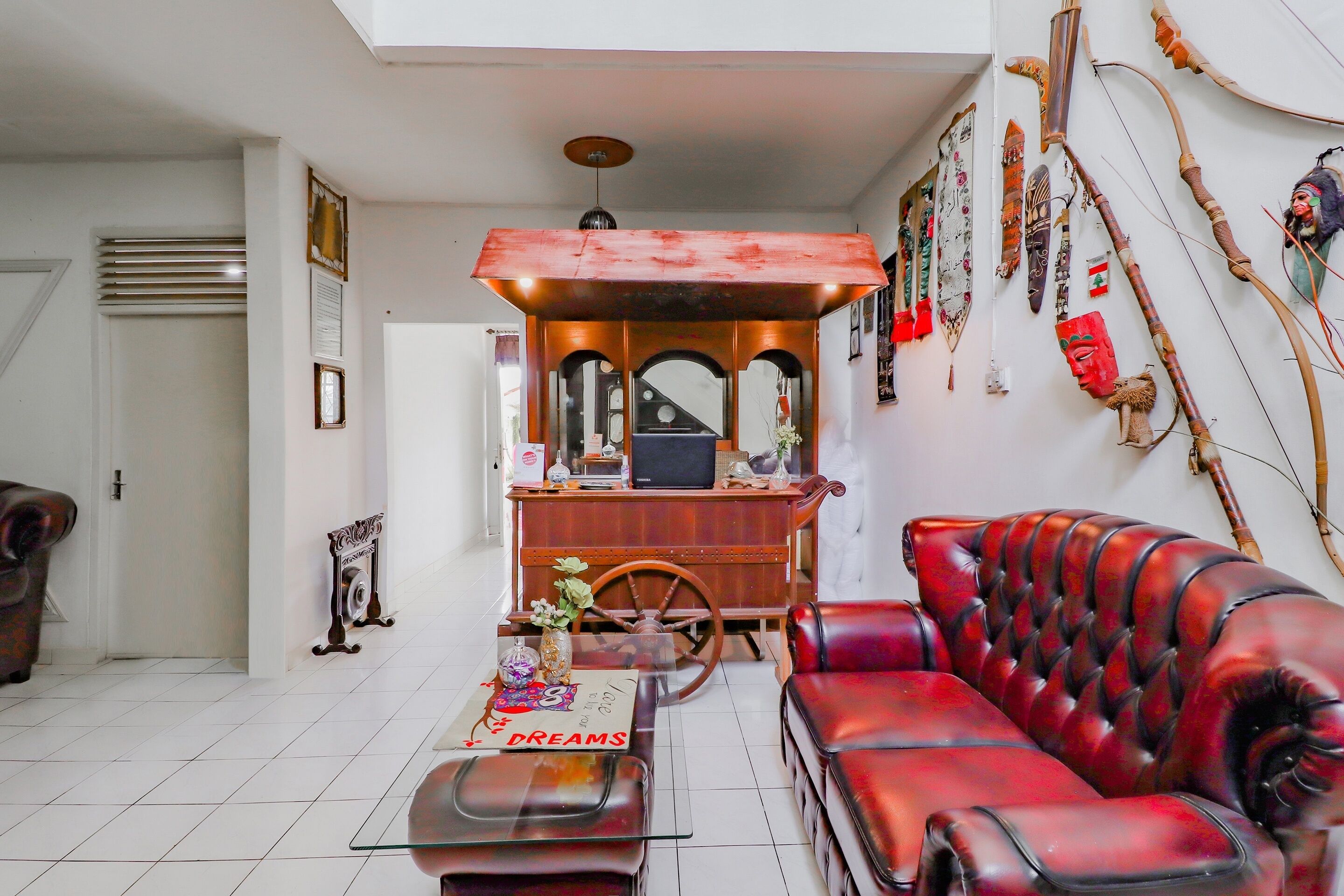 A living room with a red leather sofa, a wooden entertainment unit, and various decorative items including a wall-mounted archery set.
