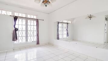 A spacious room with white tiled flooring, large windows with curtains, and a ceiling fan.